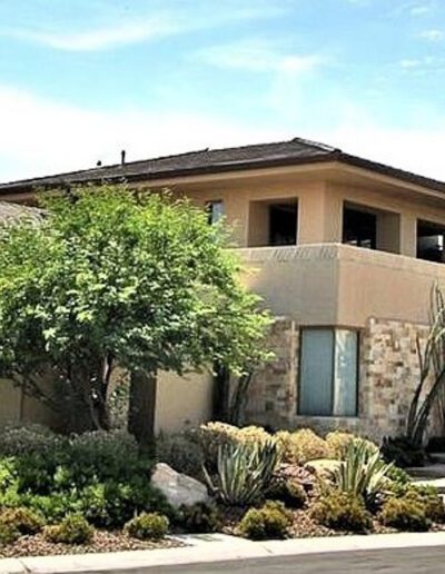 A home with cactus and bushes in front of it.