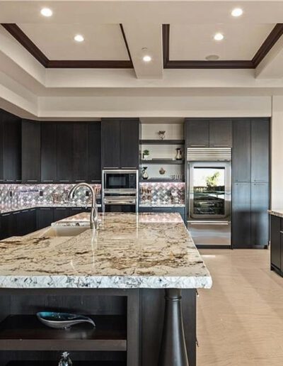 A kitchen with black cabinets and marble counter tops.