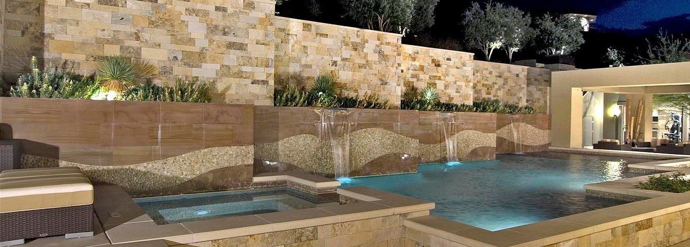 A swimming pool with a stone wall and lounge chairs.